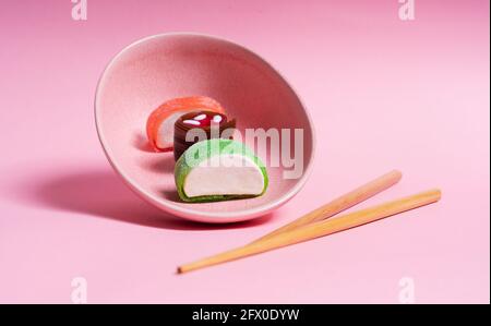 Appetitlich buntes, süßes Sushi auf Keramikplatte mit Holzplatte Essstäbchen auf rosa Hintergrund platziert Stockfoto