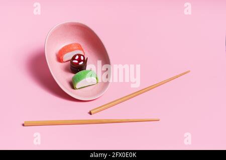 Blick von oben auf appetitlich buntes, süßes Sushi, serviert auf Keramik Teller mit Holzstäbchen auf rosa Hintergrund platziert Stockfoto