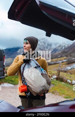 Nachdenklicher weiblicher Rucksack im Kofferraum des Autos, während man wegschaut Gegen die Berge der Gipfel Europas in Spanien Stockfoto