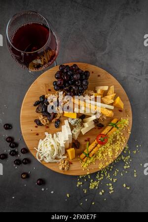 Käseplatte mit Trauben, Marmelade, Feigen, Crackern und Walnüssen auf dunklem Steingrund Stockfoto