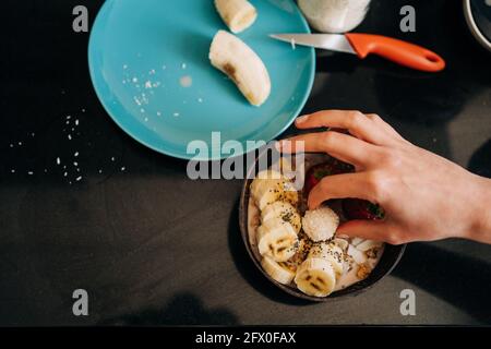 Draufsicht Ernte unkenntlich Person Belag leckeren gesunden Brei mit Bananen und Erdbeeren in der Küche Stockfoto
