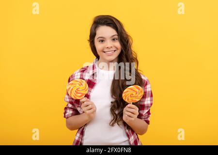 Happy teen Mädchen mit lockigen Haaren halten Lollipop Karamell Süßigkeiten auf gelbem Hintergrund, Karamell-Shop. Stockfoto