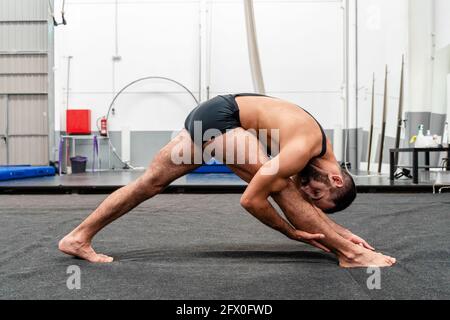 Full Body Fit flexibler Mann in Sportshorts Doing Triangle Pose und Blick auf die Kamera, während Yoga in modernen üben Fitnesscenter Stockfoto