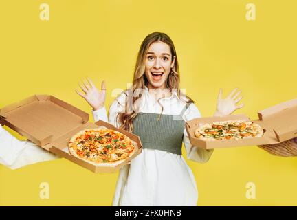 Emotional überrascht junge Frau versucht, Pizza auf gelbem Hintergrund zu wählen. Pizzalieferkonzept. Stockfoto