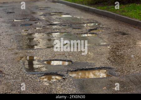 Schlaglöcher und Pfützen auf schlecht gebrochener nasser Asphaltstraße danach Rain – Vollformathintergrund Stockfoto