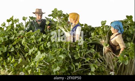 Miniaturfiguren auf einem Bauernhof. Ein Mädchen, das Pferd, ein Mann und eine Frau in der Nähe des Traktors, jemand, der die Kühe füttert, das Bauernhaus im Hintergrund. Stockfoto