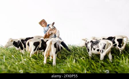 Miniaturfiguren auf einem Bauernhof. Ein Mädchen, das Pferd, ein Mann und eine Frau in der Nähe des Traktors, jemand, der die Kühe füttert, das Bauernhaus im Hintergrund. Stockfoto