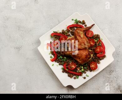 Gebackenes Hähnchen mit Linsen, сherry-Tomaten und Schalotten auf einem weißen rechteckigen Teller auf hellgrauem Hintergrund. Draufsicht, flach liegend Stockfoto