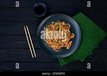 Asiatische udon-Nudeln mit Hühnergemüse und Teriyaki-Sauce auf schwarzem Holzgrund. Chinesische und japanische Küche. Stockfoto