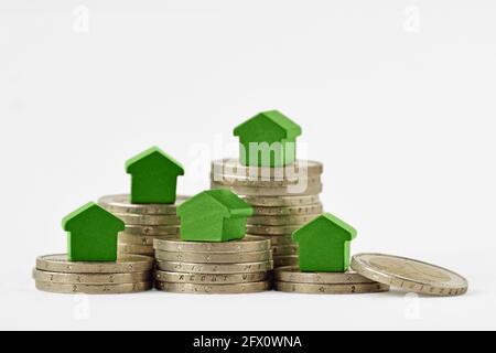 Grüne Miniaturhäuser auf Münzstapeln auf weißem Hintergrund - Konzept der Immobilieninvestition, Hypothek, Hausversicherung und Darlehen, umweltfreundliche Haus Stockfoto