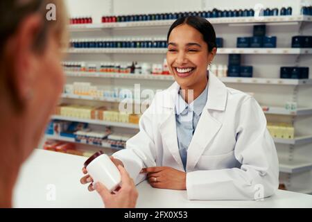 Glückliche Apothekerin in Labcoat und hinter dem Gegengeben stehend Flasche Pillen an den Kunden Stockfoto