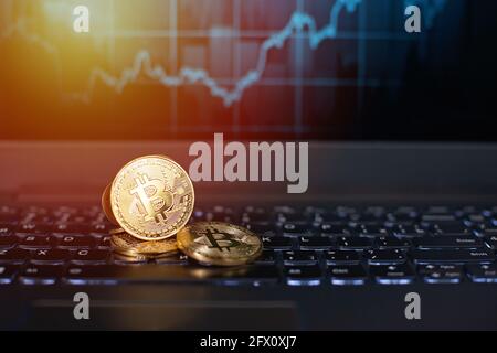 Bitcoin-Münzen auf einer Tastatur vor dem Hintergrund eines unfokussten Wachstumsgraphen. Das Konzept der virtuellen Kryptowährung. Bitcoin Mining, online BU Stockfoto