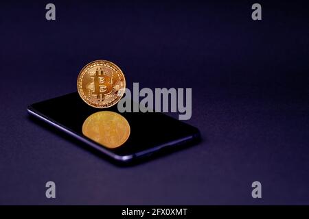 Bitcoin Goldmünze auf Smartphone-Bildschirm, Reflexion, schwarzer Hintergrund. Das Konzept der virtuellen Kryptowährung. Bergbau Bitcoins Online-Geschäft, Einkaufen Stockfoto