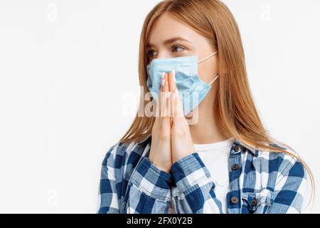 Junge Frau in medizinischer Schutzmaske, geschlossenen Augen, beten, Hände in Gebet Glauben Konzept, auf weißem Hintergrund geklammt Stockfoto