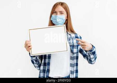 Junge Frau in Schutzmaske mit leerem Schild mit Kopie Leerzeichen auf isoliertem weißem Hintergrund Stockfoto