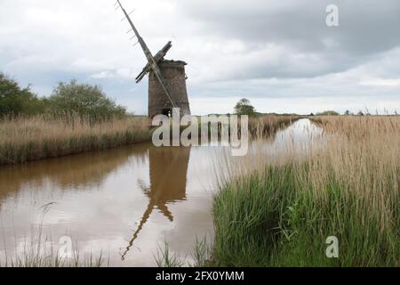 Die Landschaft der alten Ziegelwindmühle Pumpe Holz Segel reflektieren Im Flusswasser von Norfolk Broads bei Horsey East Anglia England großbritannien am Schilfufer Frühling Stockfoto