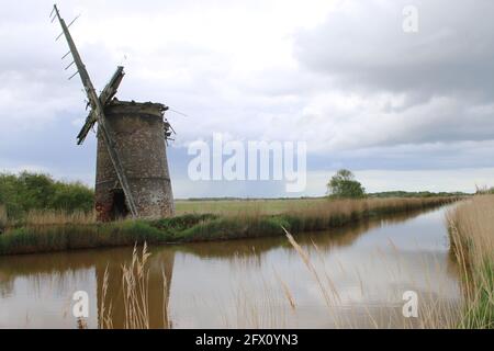 Die Landschaft der alten Ziegelwindmühle Pumpe Holz Segel reflektieren Im Flusswasser von Norfolk Broads bei Horsey East Anglia England großbritannien am Schilfufer Frühling Stockfoto