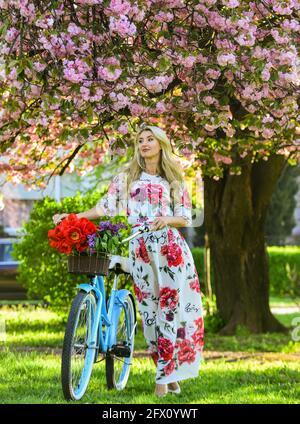 Sakura-Saison. Tourismuskonzept. Transport und Reisen. Mädchen langes Kleid Retro Cruiser Fahrrad Sakura Baum. Frühlingsferien. Frau mit Tulpen Stockfoto