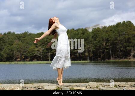 Ganzkörperprofil einer Schönheitsfrau, die ihre Arme ausstreckt und feiert Urlaub mit einem weißen Kleid in einem See Stockfoto