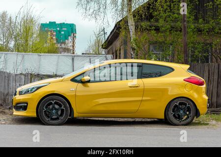 Gelbes Coupé-Auto vor dem Hintergrund eines alten Holzhauses. Tag in der Stadt, horizontale Aufnahme, Seitenansicht. Surgut, Russland - 17, Mai 2021. Stockfoto