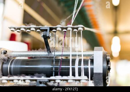 Nahaufnahme des farbigen Kaschmirwollgarns, das durch einen eingefädelt ist Zuführung auf einer handelsüblichen Strickmaschine in einem Strickwaren Fabrik Stockfoto