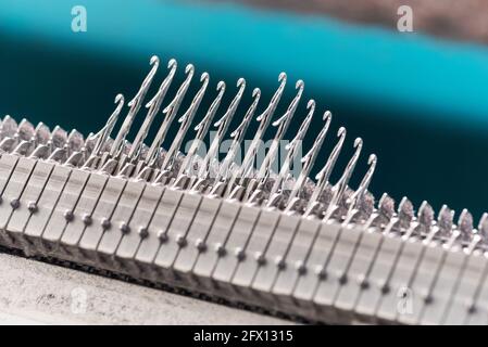 Nahaufnahme einer Reihe von hochgesteckten Stahlverriegelungen Nadeln auf einer handelsüblichen Strickmaschine in einer Strickfabrik Stockfoto