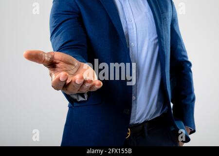 Mittelteil eines Geschäftsmannes, der ein unsichtbares Objekt gegen Grau hält Hintergrund Stockfoto