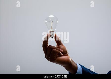 Nahaufnahme eines afroamerikanischen Geschäftsmannes, der eine Glühbirne gegen die Lampe hält Grauer Hintergrund Stockfoto