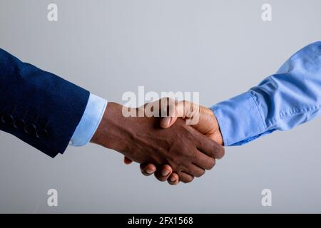 Mittelteil von zwei Geschäftsleuten, die sich vor grauem Hintergrund die Hände schüttelten Stockfoto