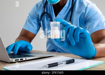 afroamerikanischer männlicher Gesundheitshelfer trägt Gesichtsmaske mit Medikamenten Container mit Laptop Stockfoto