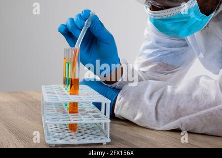 afroamerikanischer männlicher Gesundheitsarbeiter trägt Gesichtsmaske bei der Arbeit mit Chemikalien im Reagenzglas Stockfoto