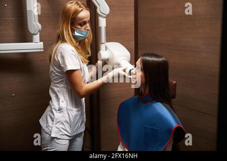 Weibliche Zahnärztin, die die zahnärztliche Röntgeneinheit beim Patienten leitet Stockfoto