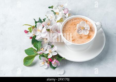 Eine Tasse Cappuccino am Morgen und ein Zweig eines blühenden Baumes auf grauem Hintergrund. Stockfoto