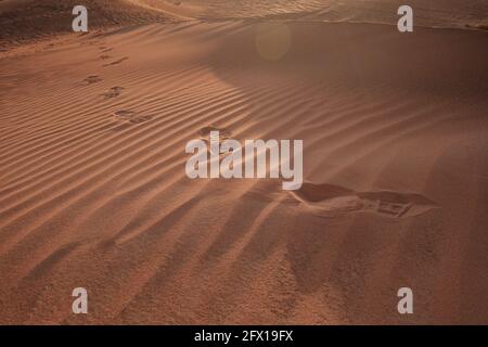Sonnenuntergang über den Sanddünen mit Fußabdrücken in der Wüste. Die Geisterstadt Al-Madam liegt etwa 60 km von Dubai City entfernt. vereinigte arabische emirate. Das Konzept Stockfoto