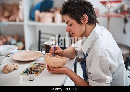 Friedlicher Keramik-Designer arbeitet an Malerei in Tonschale Stockfoto