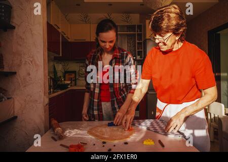 Junge Frau und ältere Mutter kochen Kekse in roten Kleidern. Stockfoto