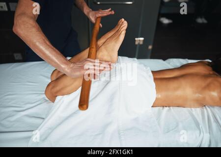 Unbekannter männlicher Masseur, der ein Holzwerkzeug in der Hand hält und macht Fußmassage in der Schönheitsklinik Stockfoto