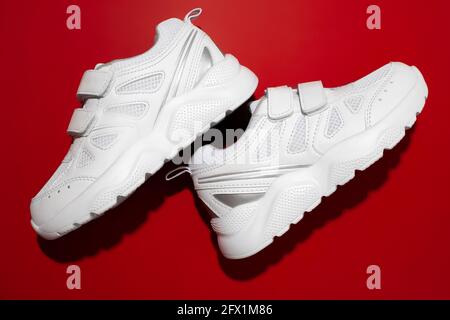 Draufsicht Nahaufnahme zwei Unisex-Laufschuhe mit der Vorderseite Teile drehten sich in verschiedene Richtungen mit harten Sommersonnenschatten Auf einem roten Hintergrund Stockfoto