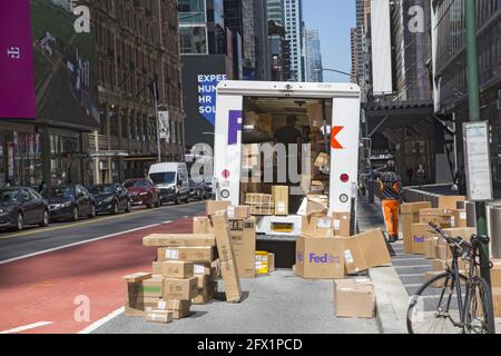FedEx-Zusteller wie die anderen großen Lieferdienste ist heutzutage aufgrund der Abschaltung von Covid-19 so beschäftigt, dass er die Straße nutzen muss, um die zahlreichen Pakete, die er zur Lieferung hat, hier in Midtown Manhattan, NYC, zu regeln. Stockfoto