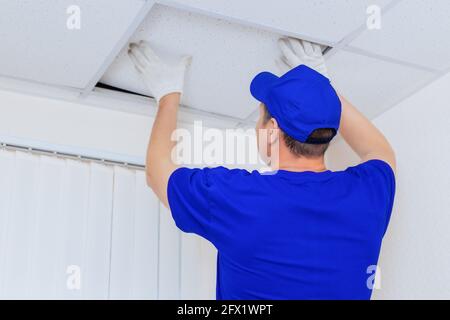 Ein Arbeiter in Overalls installiert eine Deckenfliese aus Trockenbau in einem Büroraum. Werbefoto der Dienstleistungen für die Reparatur und Dekoration der Räumlichkeiten. Modell Stockfoto