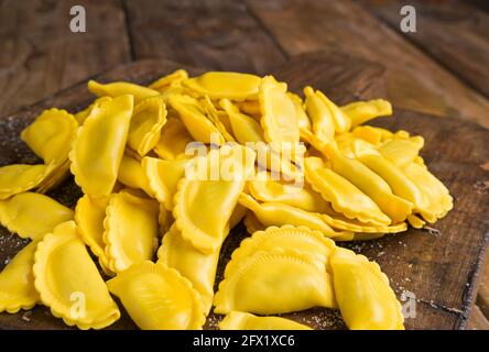 Kleine Ravioli mit Käse oder Fleisch zum Kochen in Brühe, ein traditionelles Gericht für Feiern in italien, Emilia Romagna Region. Frische hausgemachte Pasta mit Füllung auf einem Holztisch. Annäherung von oben. Stockfoto