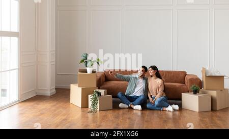 Glücklicher Mann und sitzt auf dem Boden und wählt Innenarchitektur Stockfoto