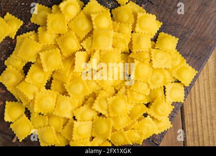 Kleine Ravioli mit Käse oder Fleisch zum Kochen in Brühe, ein traditionelles Gericht für Feiern in italien, Emilia Romagna Region. Frische hausgemachte Pasta mit Füllung auf einem Holztisch. Annäherung von oben. Stockfoto