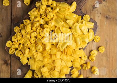 Kleine Ravioli mit Käse oder Fleisch zum Kochen in Brühe, ein traditionelles Gericht für Feiern in italien, Emilia Romagna Region. Frische hausgemachte Pasta mit Füllung auf einem Holztisch. Annäherung von oben. Stockfoto