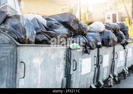 Reihen von vielen großen Metall überladenen Mülltonnen voller Schwarze Müllsäcke aus Plastik in der Nähe des Wohngebäudes in der Stadt Innenstadt oder Vorstadtbereich Stockfoto