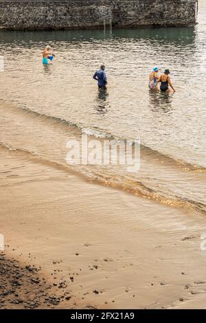 Menschen betreten das Wasser unter einem seltsamen Licht, das durch den Rauch eines Waldbrands verursacht wird, der die Sonne blockiert, Playa San Juan, Teneriffa, Kanarische Inseln, Spanien Stockfoto