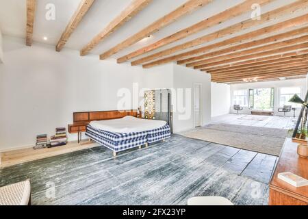 Komfortables Bett mit weißer Decke in minimalistischem, geräumigen Zimmer Haus mit Holzbalken an der Decke Stockfoto