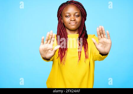 Afrikanische Frau mit Dreadlocks in einem gelben Pullover hält sie fest Hände vor ihr Stockfoto