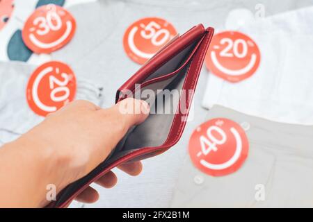 Weibliche Hände halten leere Geldbörse Hintergrund mit Kleidung mit Rabatt-Etiketten Stockfoto
