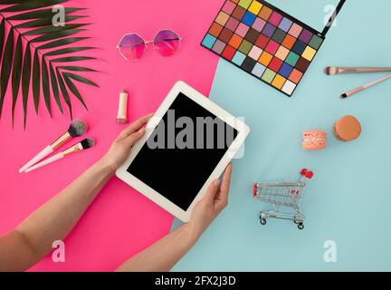 Modell mit leerem Tablet-Bildschirm in weiblichen Händen und verschiedenen Kosmetikartikeln, Sonnenbrille auf buntem Hintergrund, Draufsicht Stockfoto